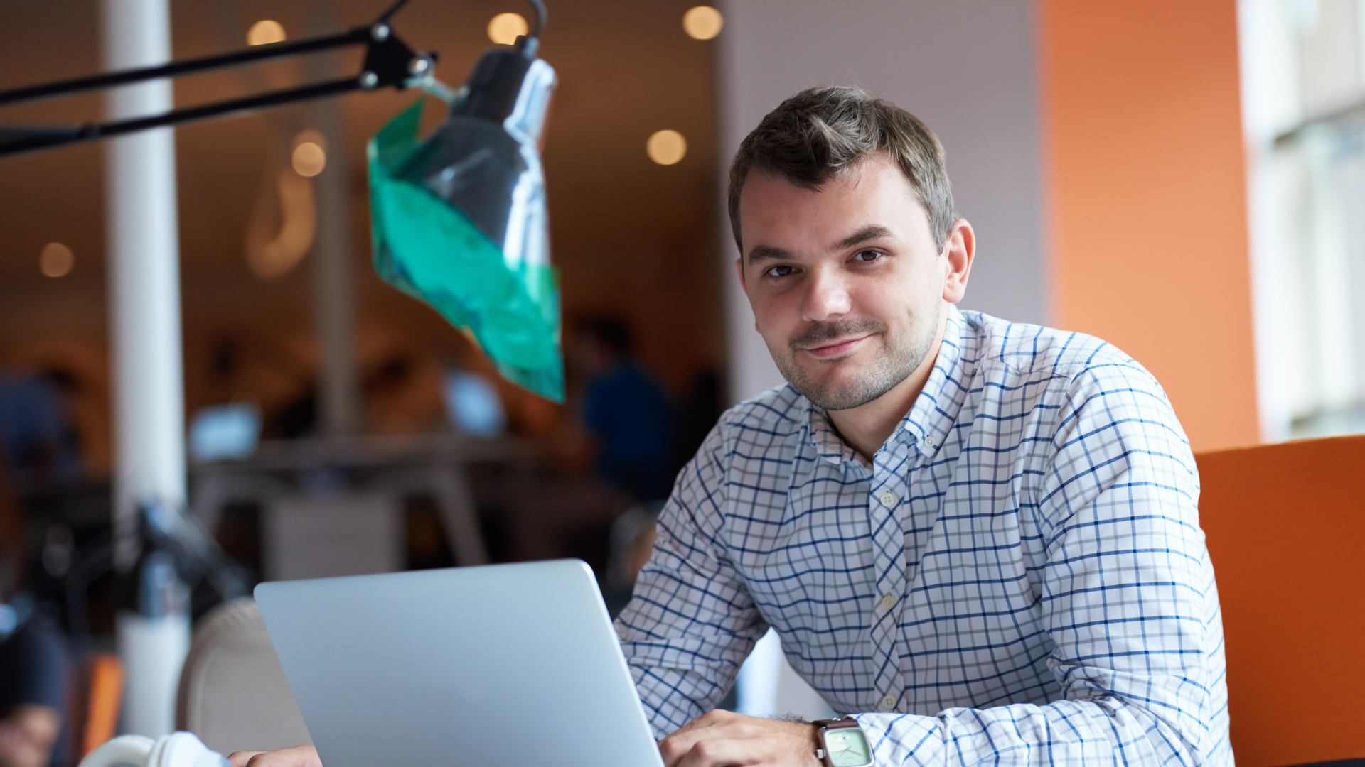 Mies istuu tietokoneen äärellä ja hymyilee kameralle.