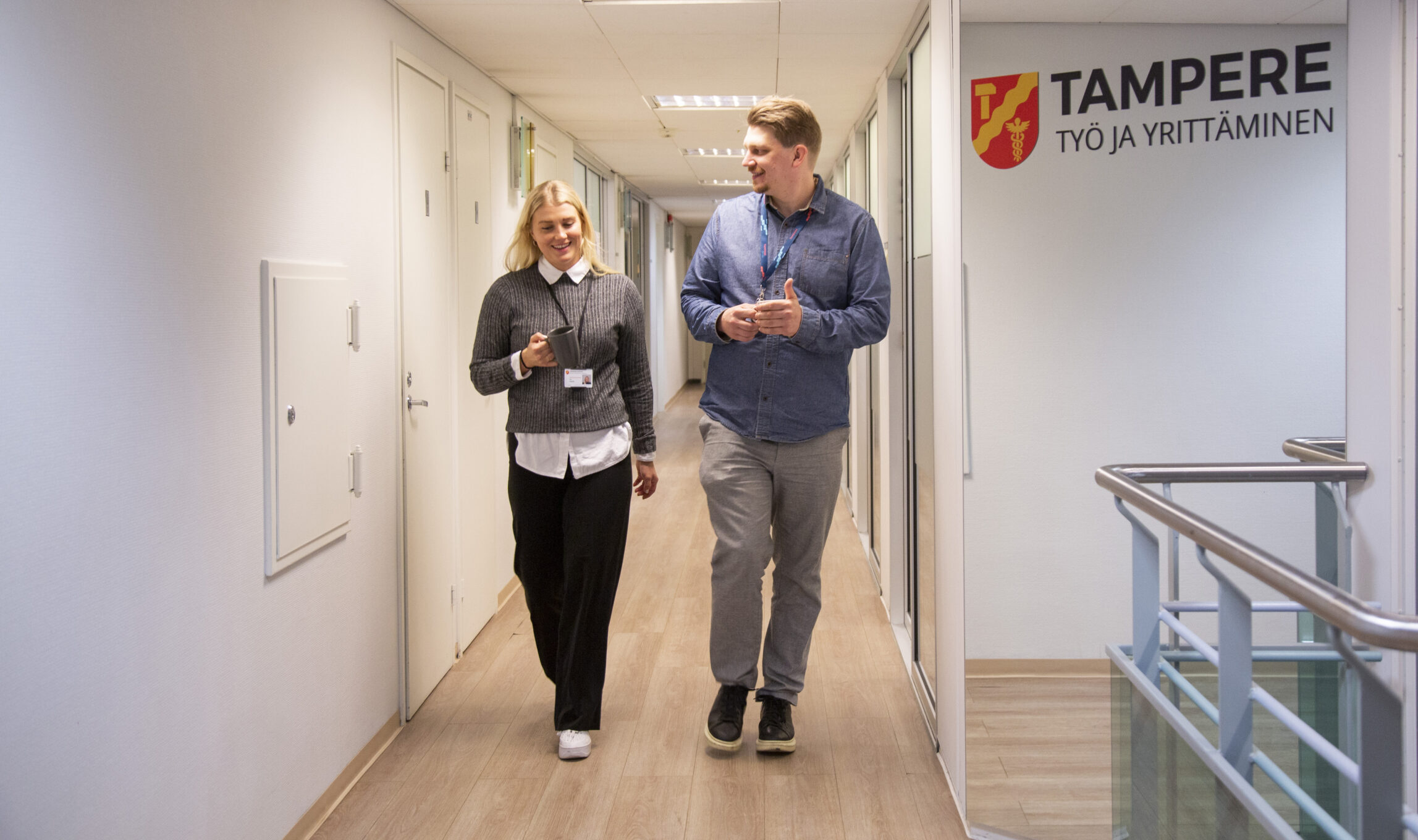 Kaksi työllisyys- ja kasvupalvelujen työntekijää kävelee toimistotilojen käytävällä. He juttelevat toisilleen ja hymyilevät