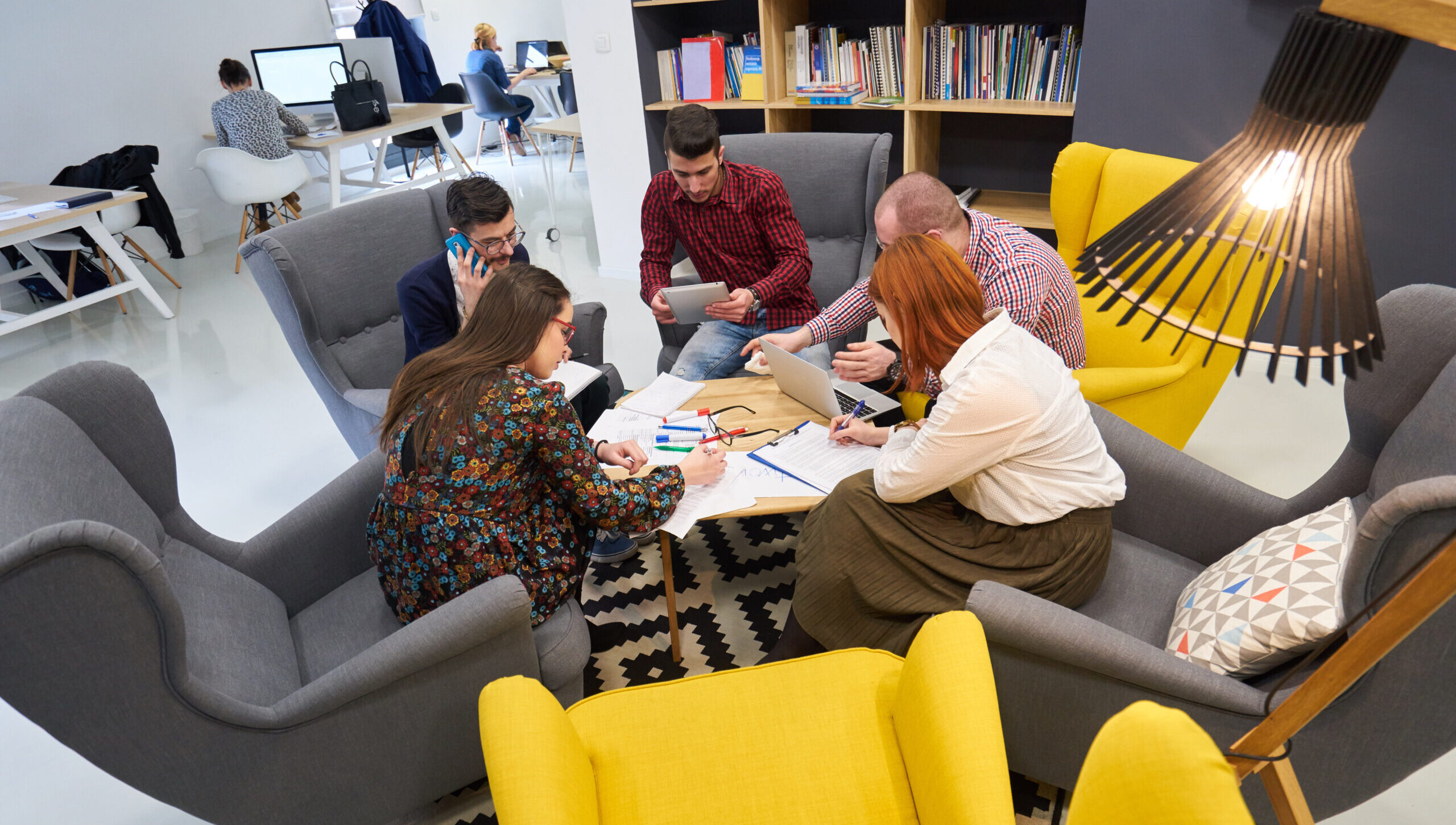 Viisi henkilöä istuu pöydän ääressä, jolla on paljon erilaisia papereita. He katsovat papereita ja toisiaan.