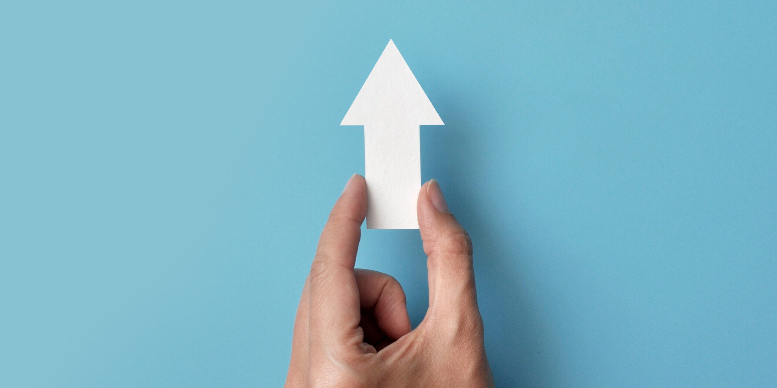 Käsi pitelee pientä valkoista nuolta, joka osoittaa ylöspäin.