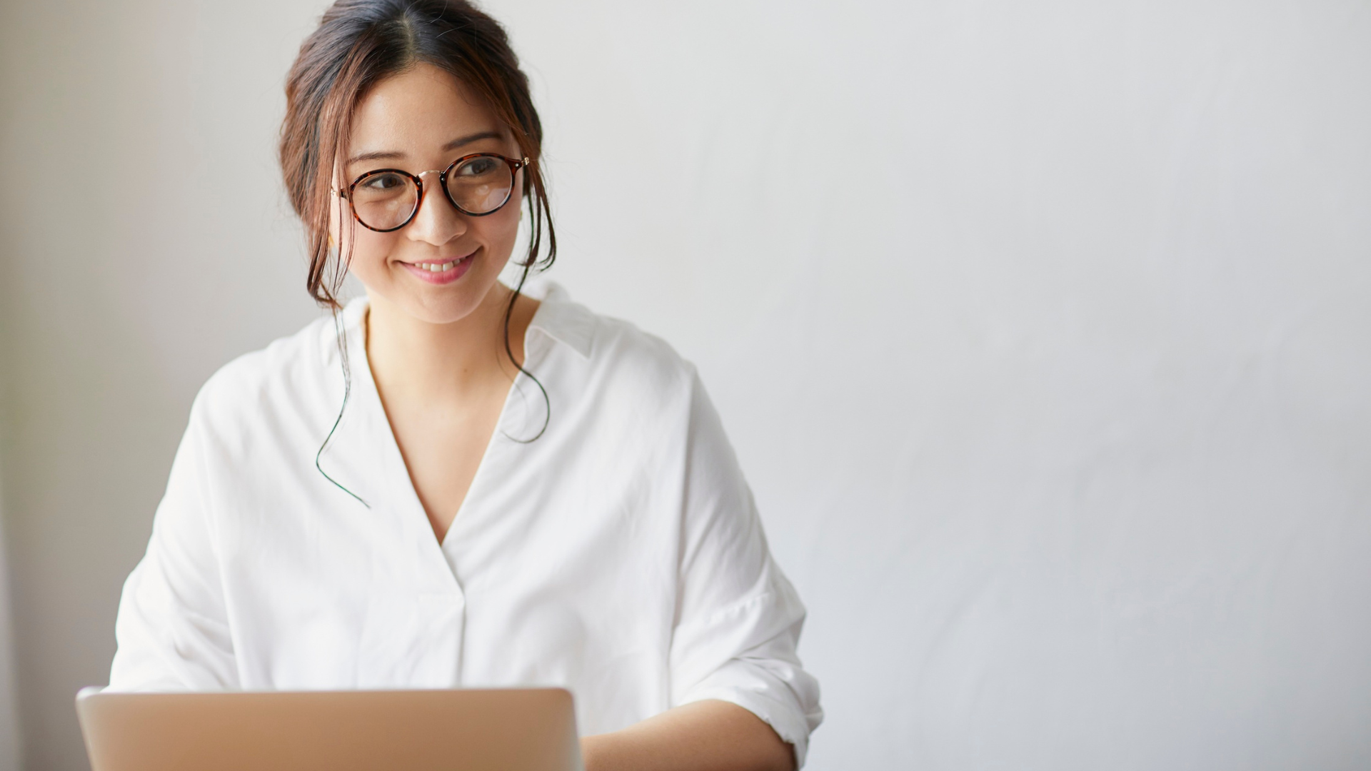 Henkilö istuu kannettavan tietokoneen edessä ja hymyilee.