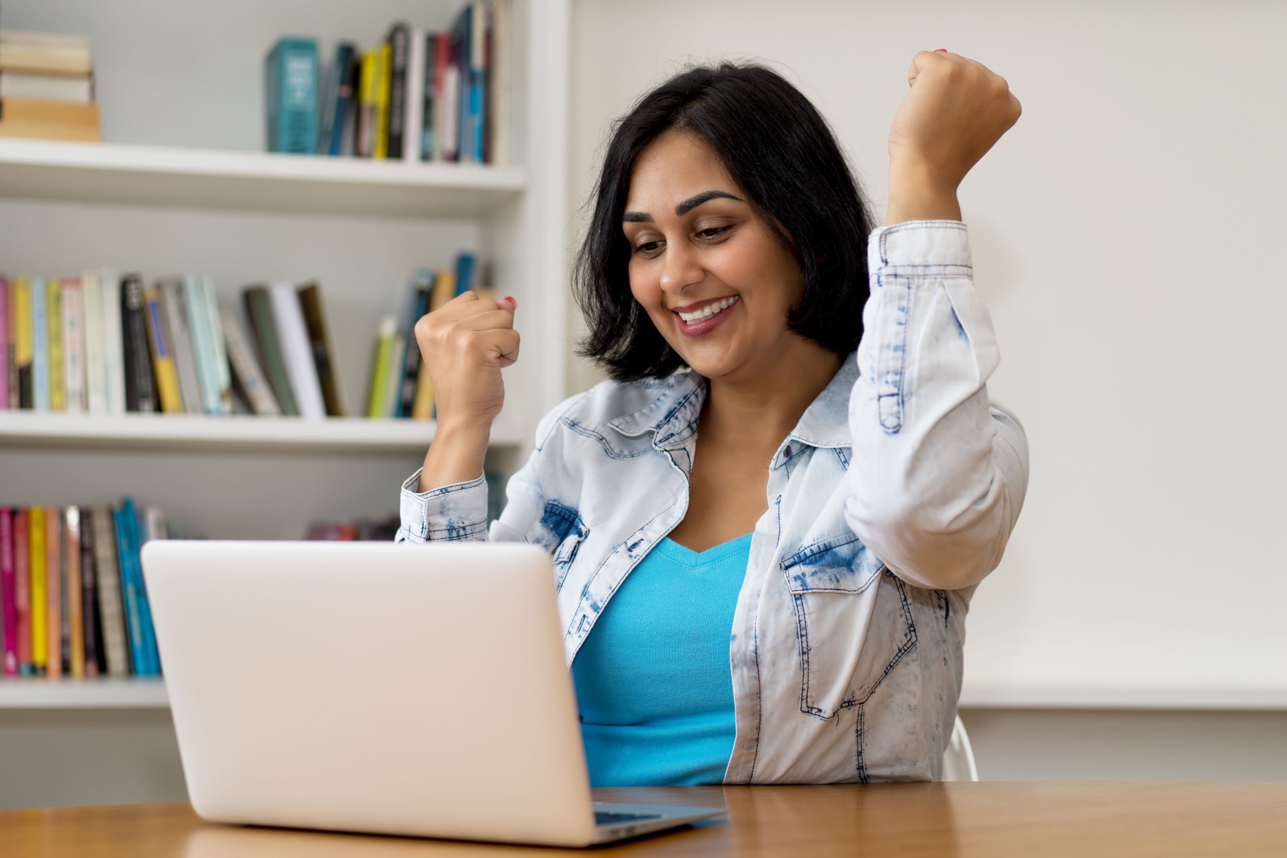 nainen katsoo tietokonetta hymyillen ja heiluttaa käsiään.